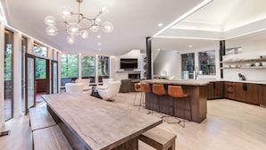Een ruime keuken met een groot eiland, moderne barstoelen en een eethoek met een houten tafel en stoelen.
