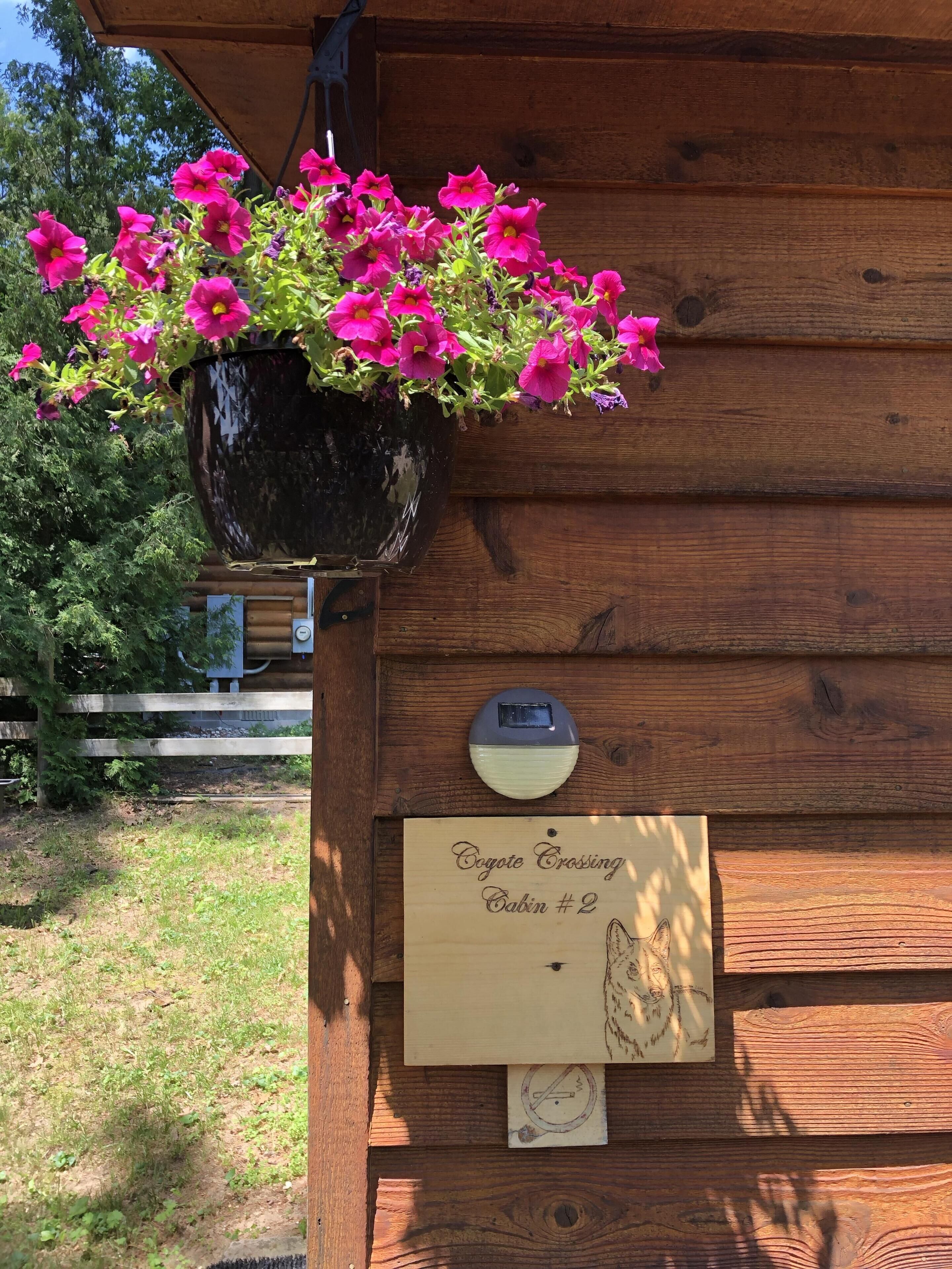 Uma cabana de madeira com um vaso de flores pendurado, uma placa de número da cabana e um interfone.