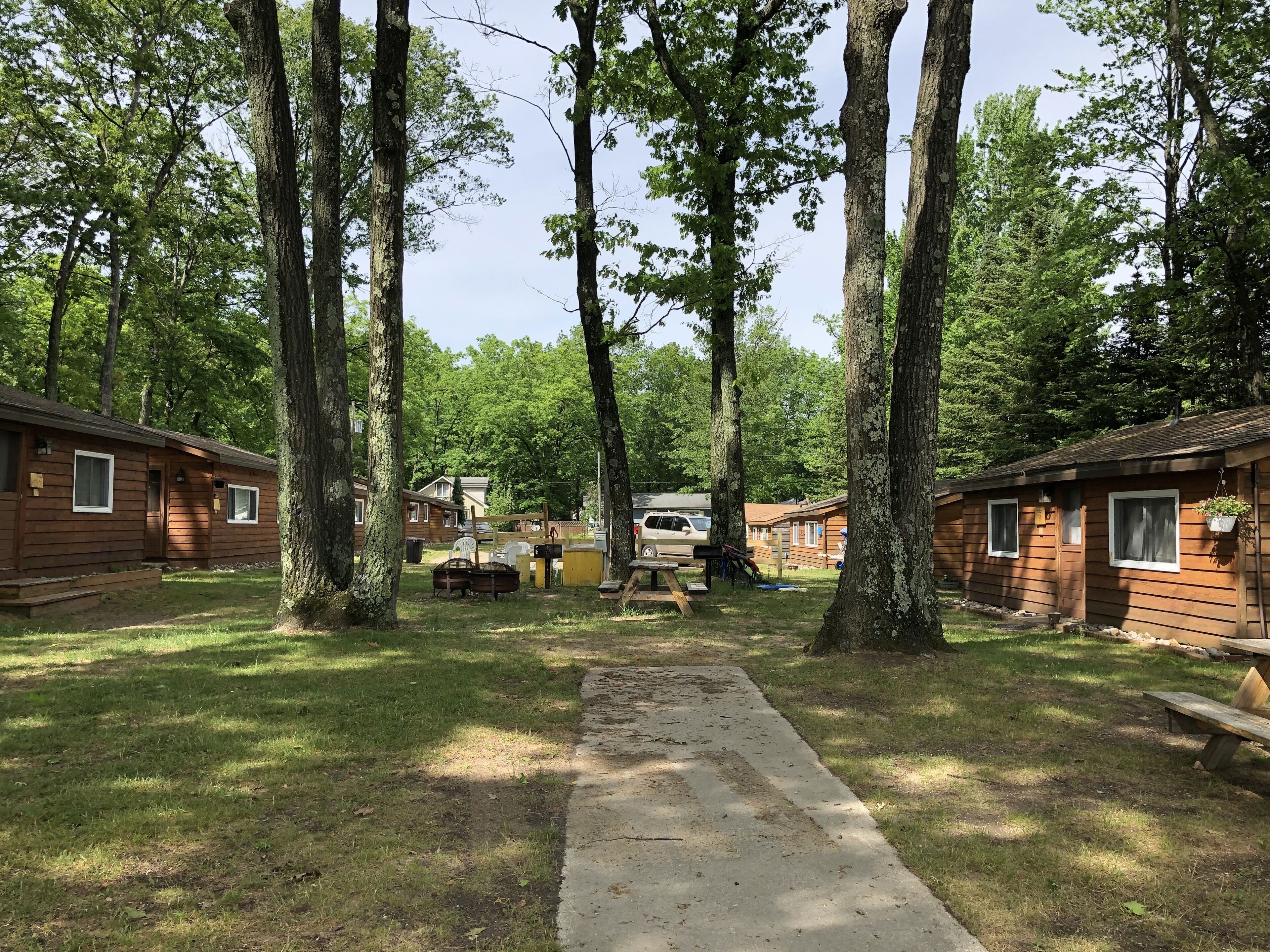Un camping con cabañas de madera, un camino de hormigón y mesas de picnic.