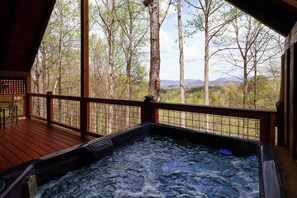 A hot tub on a wooden deck with a view of trees and mountains.