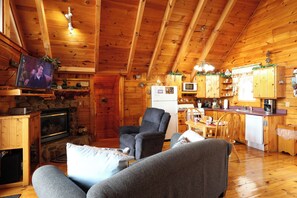 A cozy cabin interior with a fireplace, a television, a dining area, and a kitchen.