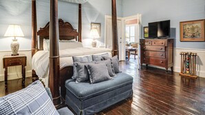A bedroom with a four-poster bed, a bench, a dresser, and a television.