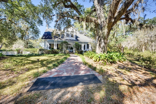 A large house with a porch, surrounded by trees and a stone pathway.