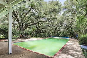 A swimming pool with a red border, surrounded by trees and a covered patio area.