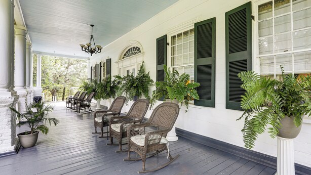 A porch with wicker rocking chairs, potted plants, and a white column.