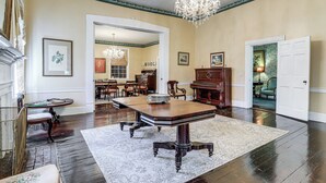 A spacious room with a large wooden dining table, a chandelier, and a piano.
