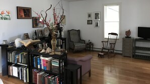 A living room with a bookshelf, a pink armchair, a wooden coffee table, and a vase with branches.