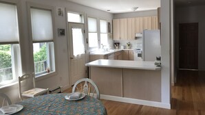 A modern kitchen with wooden cabinets, a white countertop, and a built-in oven. There is a dining area with a table set for two and a chair.