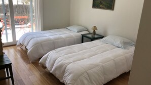 A room with two beds, a table, and a painting on the wall.