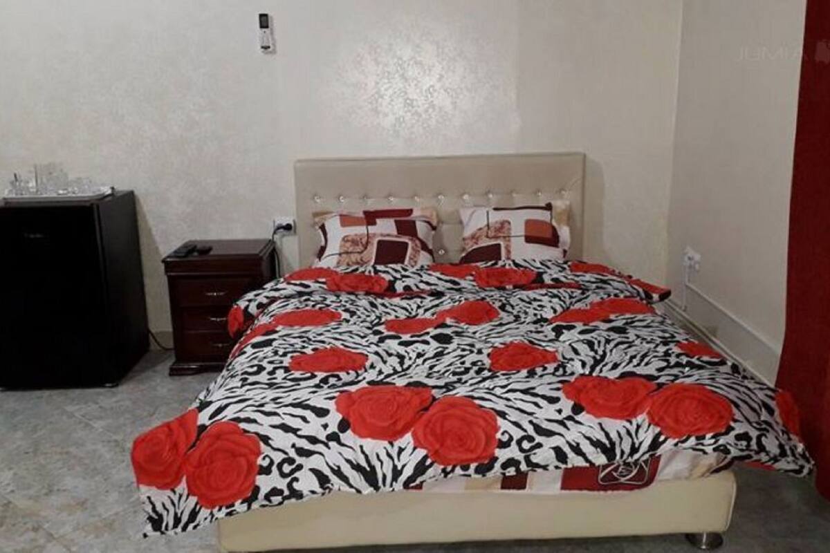 Een bed met een bedspreider met zebraprint en rozenmotief, een kleine donkere dressoir en een rood gordijn.