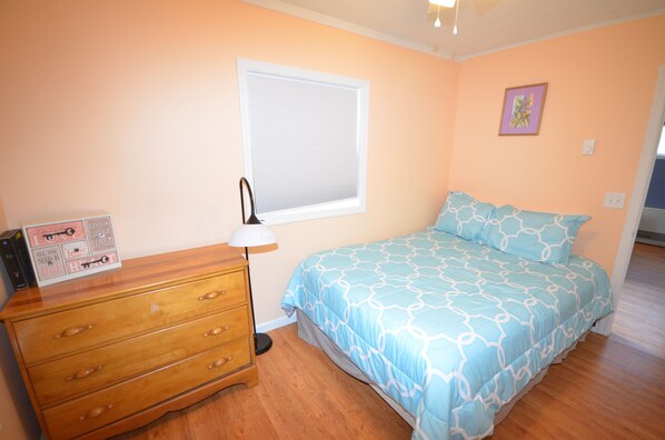 A bedroom with a bed, dresser, window, and a framed picture on the wall.