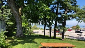 A picnic table in a grassy area with trees and a parking lot in the background.