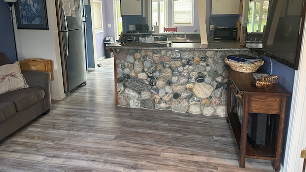 A modern kitchen with a stone island, a refrigerator, and a dining area with a couch.