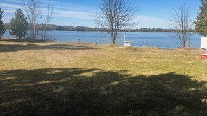 A grassy area with a dock extending into a lake, surrounded by trees and a clear sky.