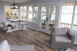 A dining area with a table and benches, a wicker chair, and a view of the outdoors through large glass doors.