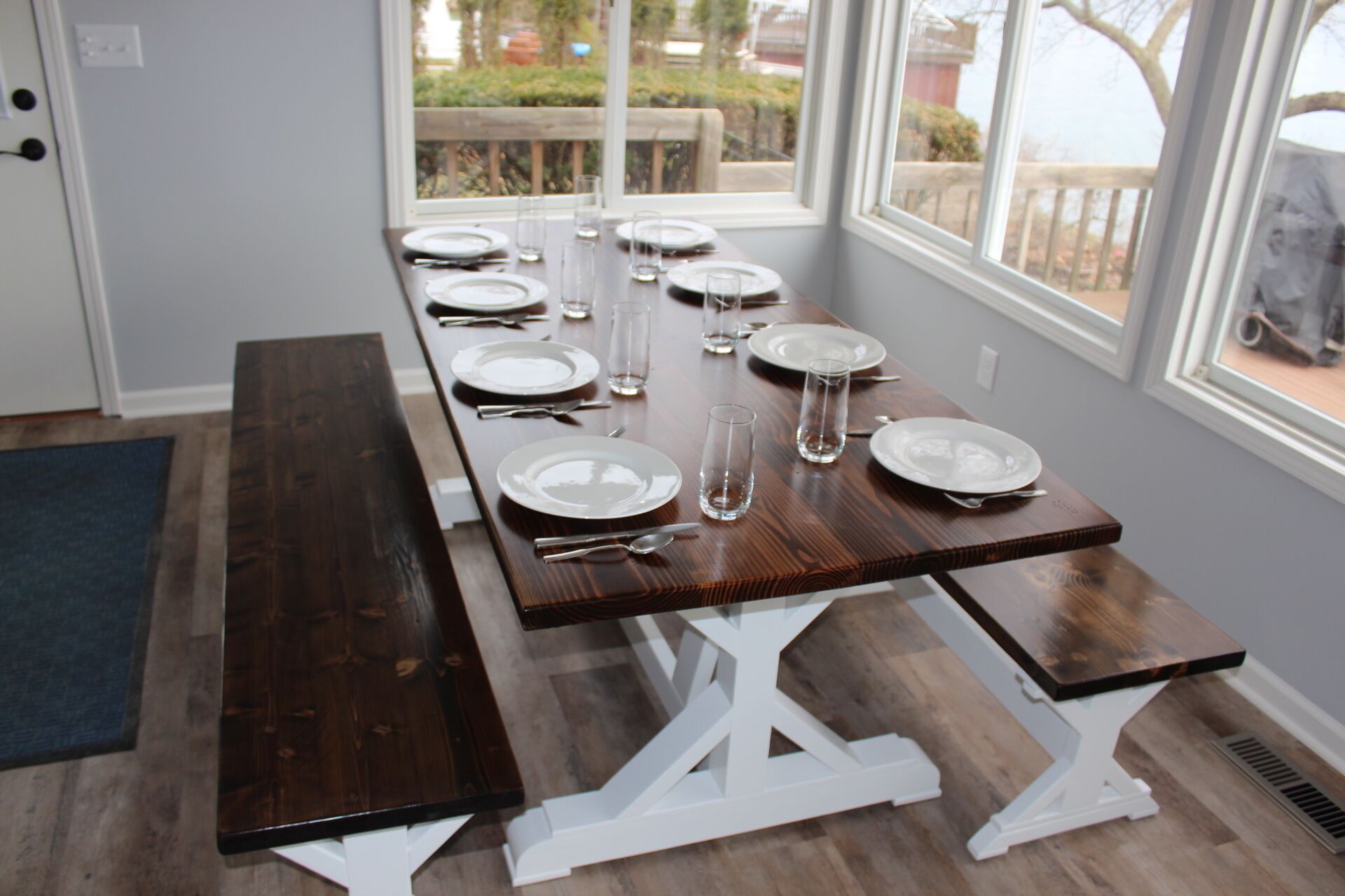 Une table à manger est dressée avec des assiettes, des verres et des couverts, et est placée près d’une fenêtre donnant sur l’extérieur.
