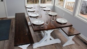 A dining table set with plates, glasses, and cutlery, positioned near a window with a view of the outdoors.