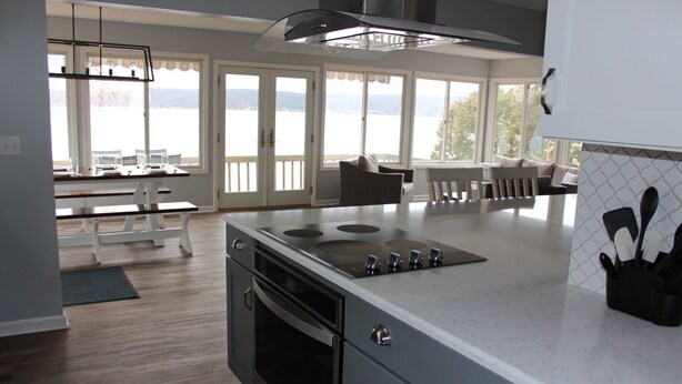 A modern kitchen with a large island, built-in oven, and a view of the outdoors through large windows.