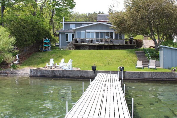 A dock leading to a house with a deck and outdoor seating.