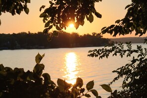 A sunset over a calm body of water with trees framing the view.
