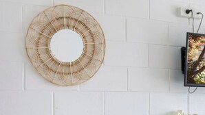 Een witte bakstenen muur met een ronde wanddecoratie van geweven materiaal, een kleine witte tafel met twee stoelen, en een plank met decoratieve objecten.