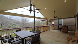Une terrasse extérieure couverte, dotée d’une table et de chaises, d’un ventilateur de plafond et offrant une vue sur le paysage environnant.