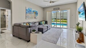 Un soggiorno moderno con un divano componibile, una ventola a soffitto, un quadro di grandi dimensioni e vista su una piscina.