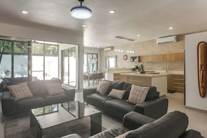 A modern living room with a glass coffee table, black sofas, and a dining area with chairs. - 1 Mi to Beach: Luxe Playa Del Carmen Home w/ Pool (Playa Del Carmen)