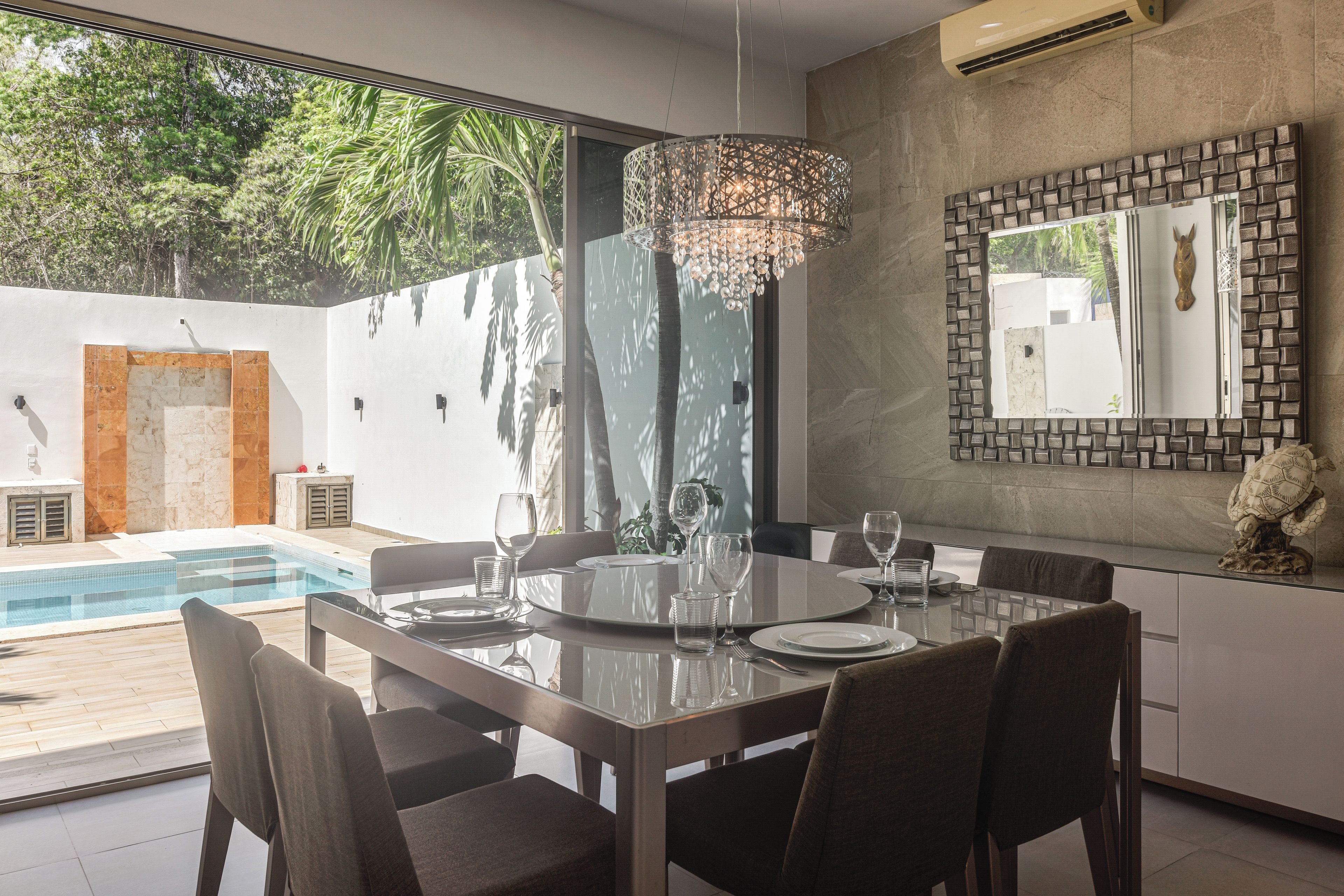 Een moderne eethoek met een glazen tafel, stoelen en een decoratieve kroonluchter.