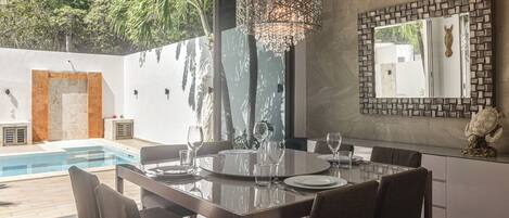 A modern dining area with a glass table, chairs, and a decorative chandelier.