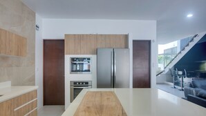 A modern kitchen with a wooden countertop, stainless steel appliances, and a view of a staircase leading to a balcony.