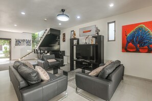 Una sala de estar moderna con un sofá de cuero negro, un televisor de pantalla plana y una escalera que conduce a un nivel superior.