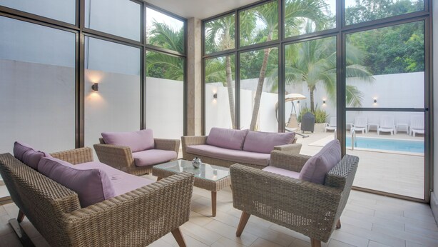 A sunlit indoor space with wicker furniture and large windows overlooking a pool and greenery.