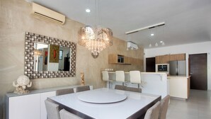 A modern kitchen with a central island, a dining area with a round table, and a large chandelier.