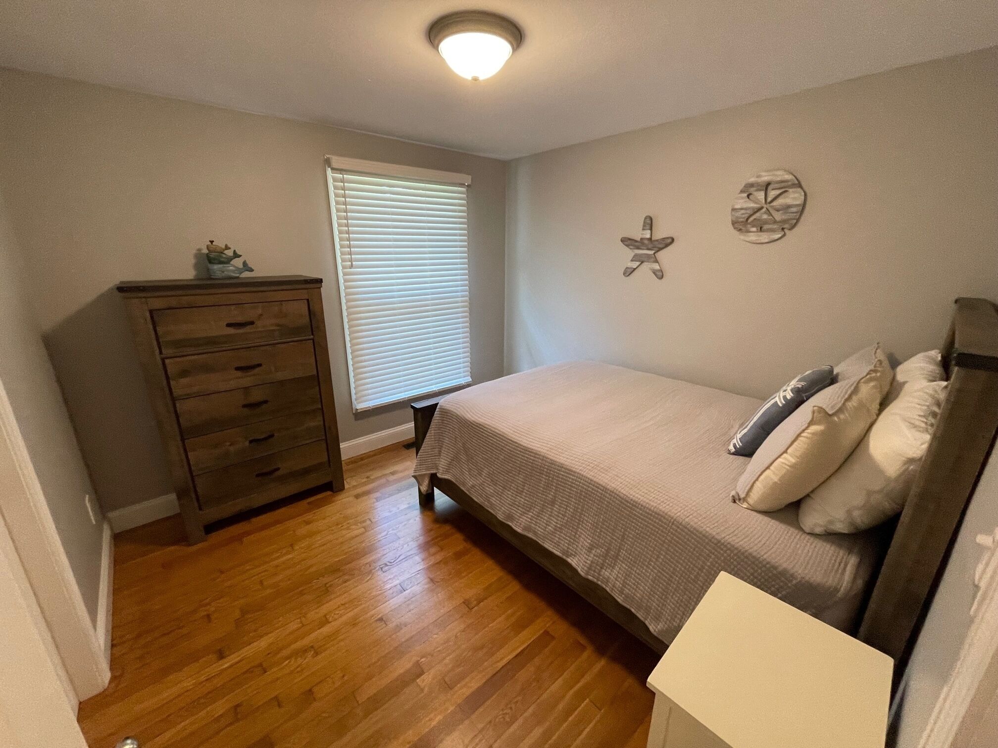 A bedroom with a bed, a dresser, a window with blinds, and wall decorations.