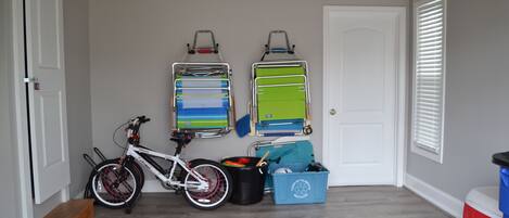 A room with a bicycle, two wall-mounted storage racks, a blue mat, a trash bin, and a cooler.