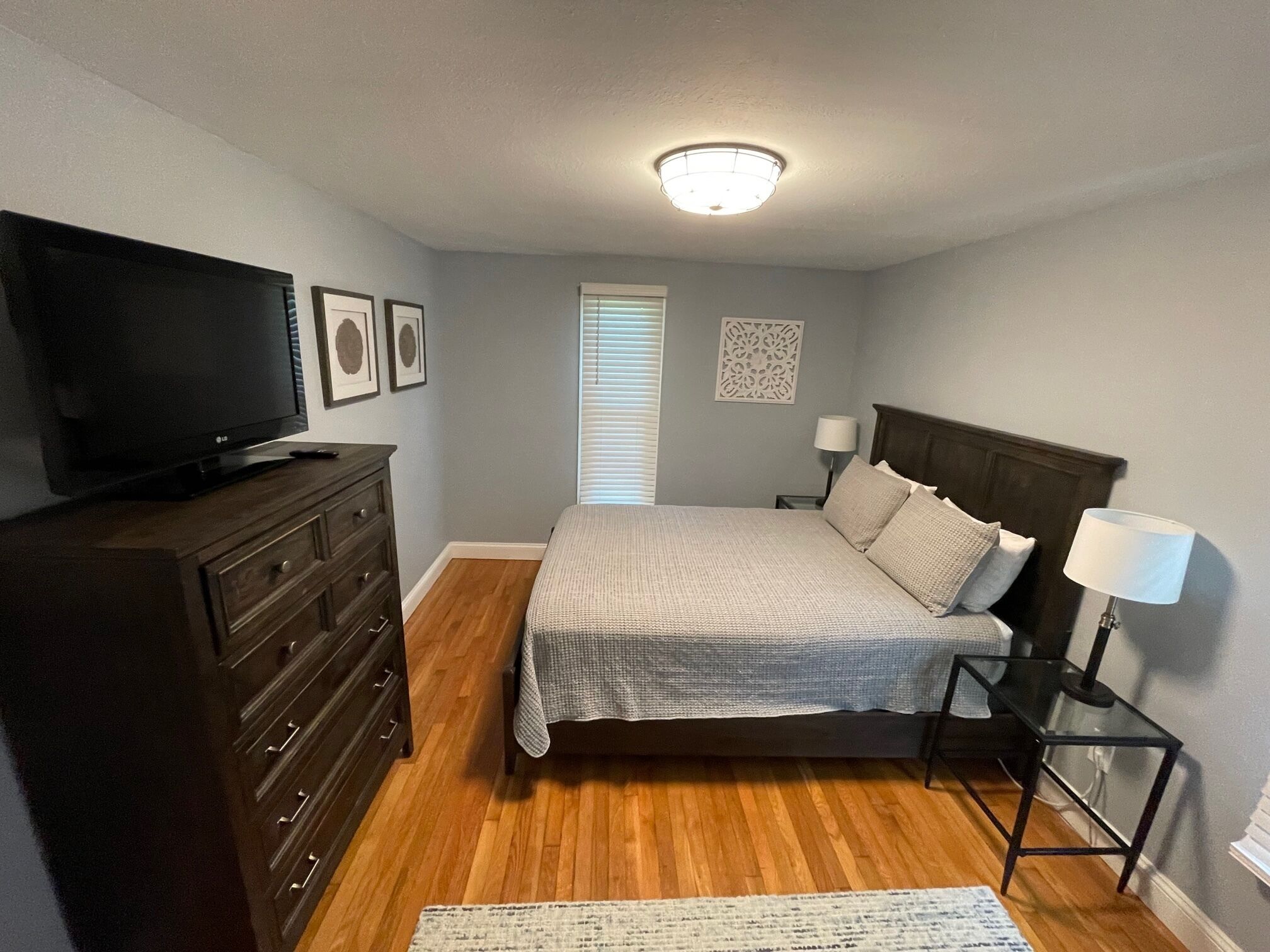 Een slaapkamer met een bed, een dressoir, een televisie en bedlampjes.