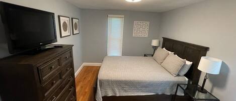Een slaapkamer met een bed, een dressoir, een televisie en bedlampjes.