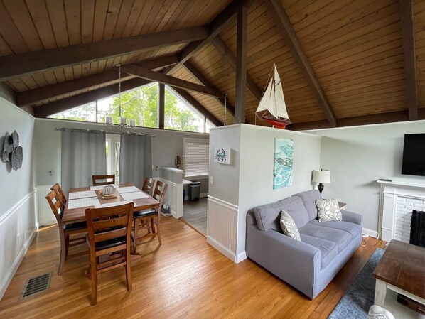 A spacious living area with a wooden ceiling, a grey sofa, a dining table with chairs, and a fireplace.