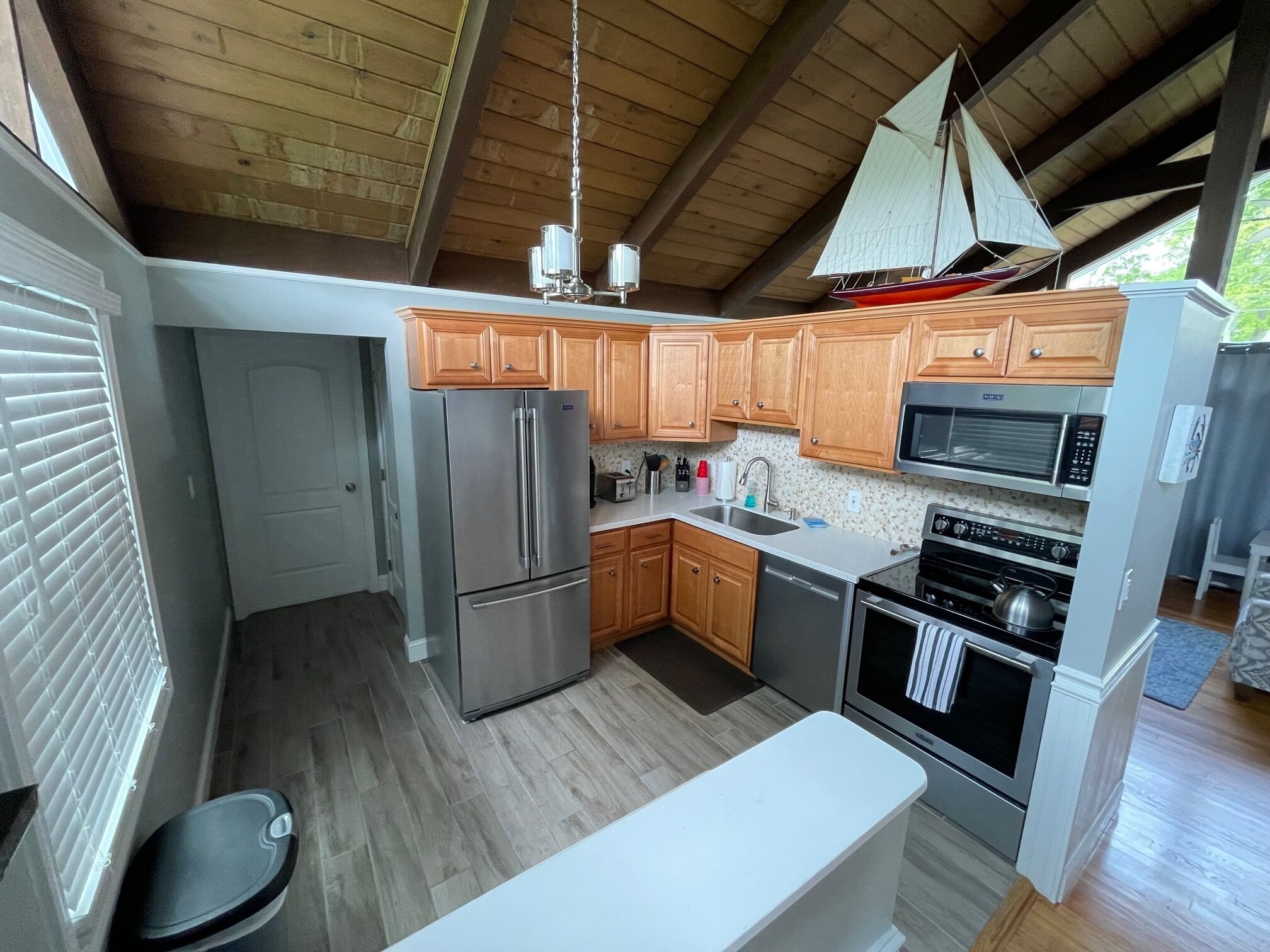 Una cocina compacta con armarios de madera, electrodomésticos de acero inoxidable y una encimera blanca.