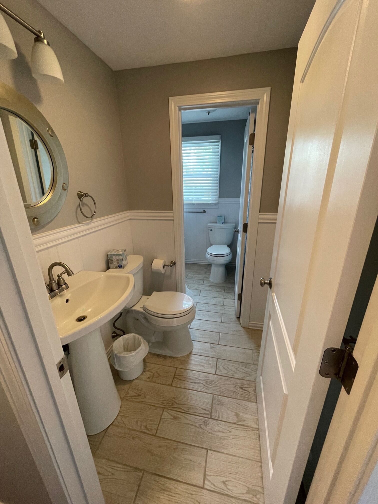 Ein Badezimmer mit Waschbecken, Toilette und Bidet. Über dem Waschbecken befindet sich ein Spiegel und über der Toilette ein Fenster. Der Boden ist mit Fliesen ausgelegt.