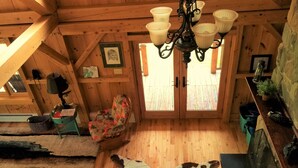 A cozy cabin interior with wooden walls, a floral armchair, a rug, and a ceiling light fixture. - Beautiful, Peaceful Lakefront Home in woods. Canoe, Kayaks, ATV trail access. (Sangerville)
