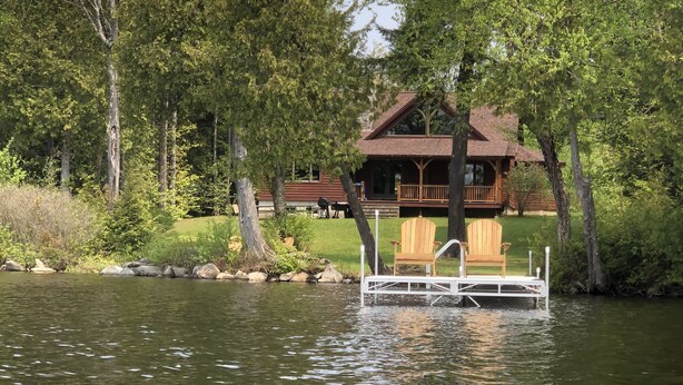 A cabin with a dock extending into a lake, surrounded by trees. - Beautiful, Peaceful Lakefront Home in woods. Canoe, Kayaks, ATV trail access. (Sangerville)