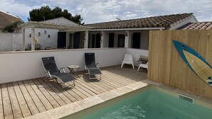 A covered outdoor swimming pool with lounge chairs and a wooden deck.