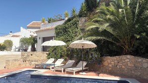 Una piscina con lettini e ombrelloni, circondata da mura in pietra e vegetazione.