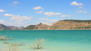 Paesaggio costiero con acque turchesi cristalline, una spiaggia sabbiosa e una collina con edifici sullo sfondo.