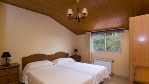 Un dormitorio con dos camas, techo de madera, una ventana con vistas a árboles, un radiador y un armario de madera.