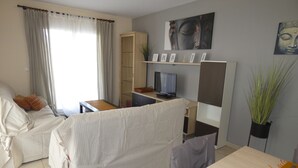 A living room with a sofa, a TV, a bookshelf, and a dining table.
