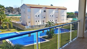 A residential building with a swimming pool, a balcony with a glass railing, and a well-maintained lawn.
