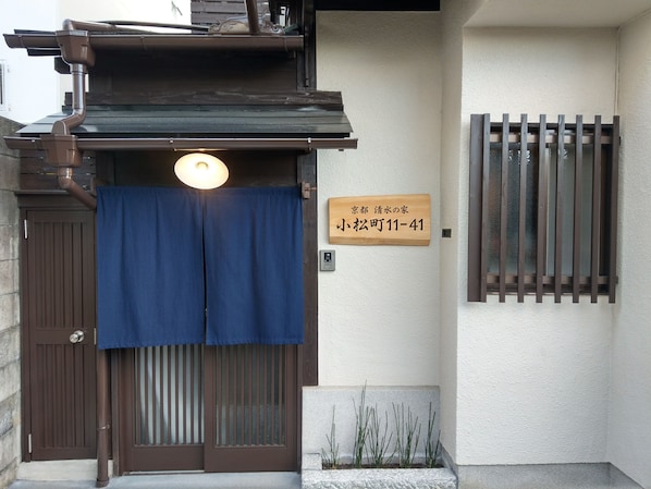A traditional Japanese entrance with a sliding door, a signboard, and a small window with bars.
